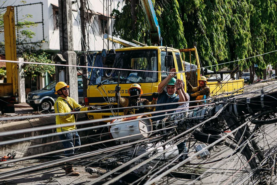 Utility workers conduct repairs on fallen power lines with heavy machinery on a sunny day.