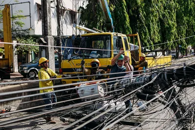 Utility workers conduct repairs on fallen power lines with heavy machinery on a sunny day.