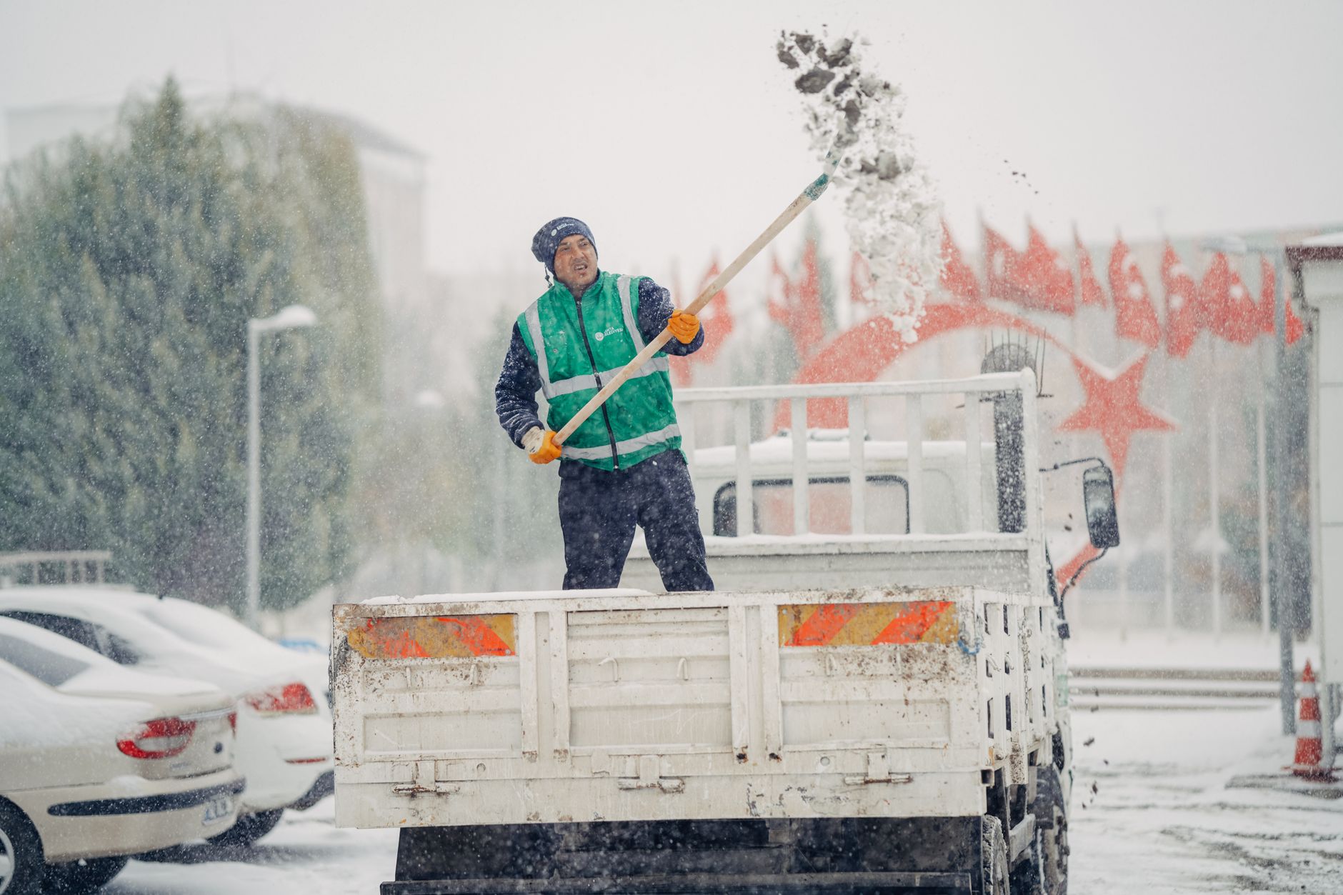 A worker shovels snow off a truck during a snowy winter day, showcasing winter work effort.