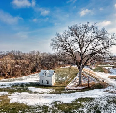 A serene rural scene in Kellogg, MN, featuring a lone house amidst snowy fields and bare trees.
