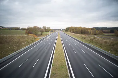 A serene image of an empty highway stretching through a peaceful countryside under a cloudy sky.